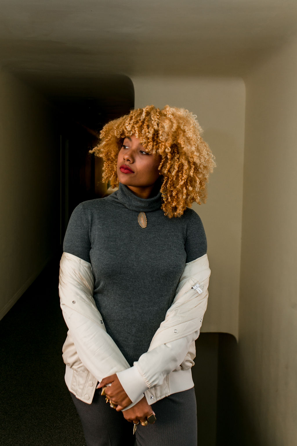 woman with blonde curly hair wearing a white bomber jacket