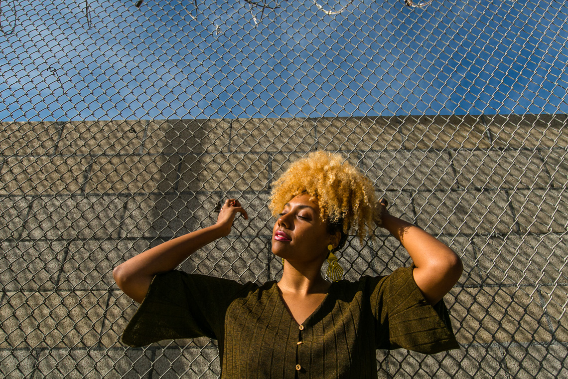 blonde curly hair-fence-model-natural lighting-outdoor lighting-h&m top